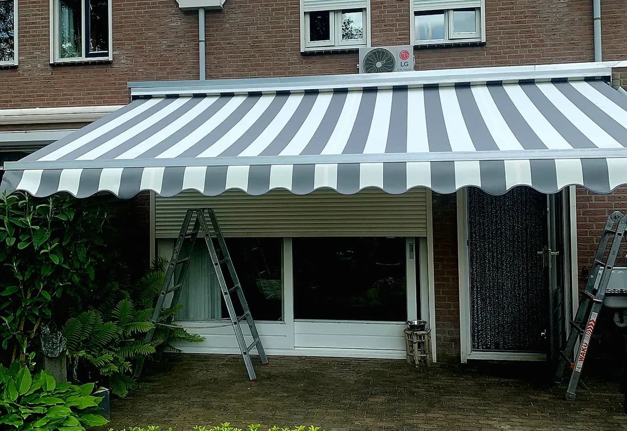 Grijs-wit gestreept knikarmscherm boven een terras