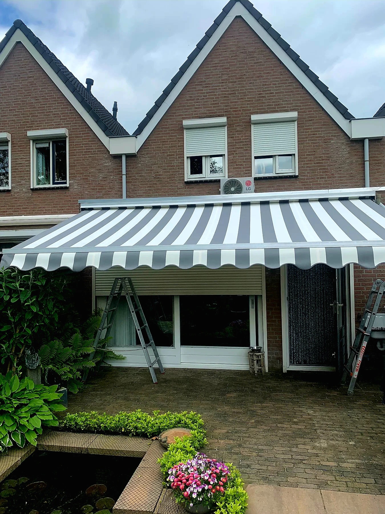 Grijs-wit gestreept knikarmscherm boven een terras