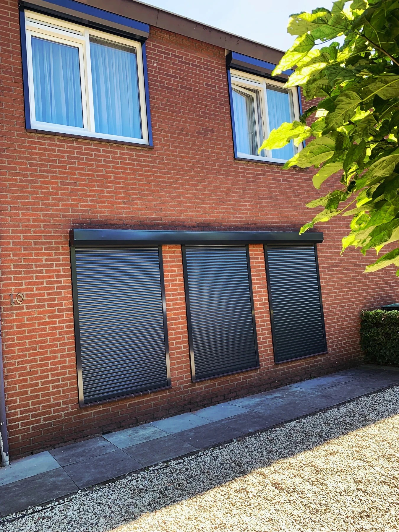 Drie antracietkleurige rolluiken aan een bakstenen gevel